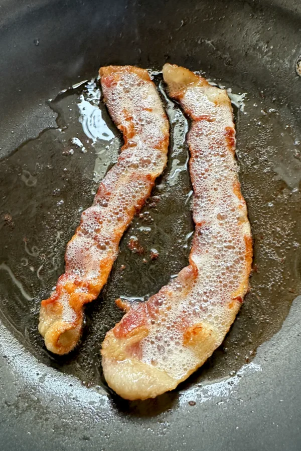 two strips of bacon sizzling in a skillet 