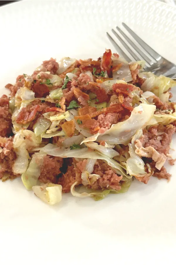 fried corned beef and cabbage on a white plate with a fork