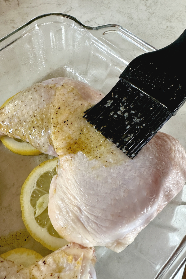 brushing oil on skin for lemon roasted chicken leg quarters