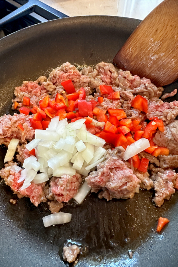 raw ground beef diced red peppers and onions in skillet