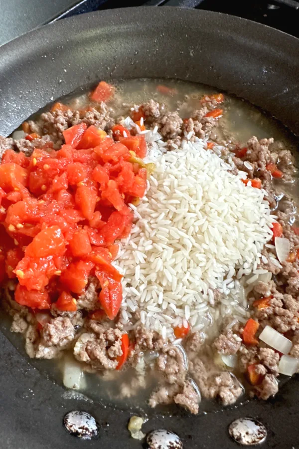 rotel tomatoes in skillet with meat and rice grains
