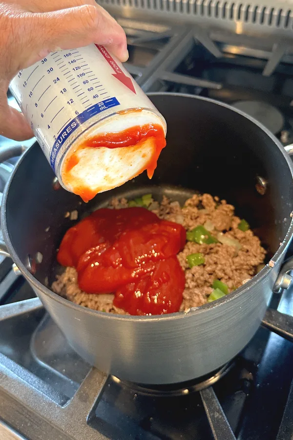 pouring ketchup over cooked ground beef. 