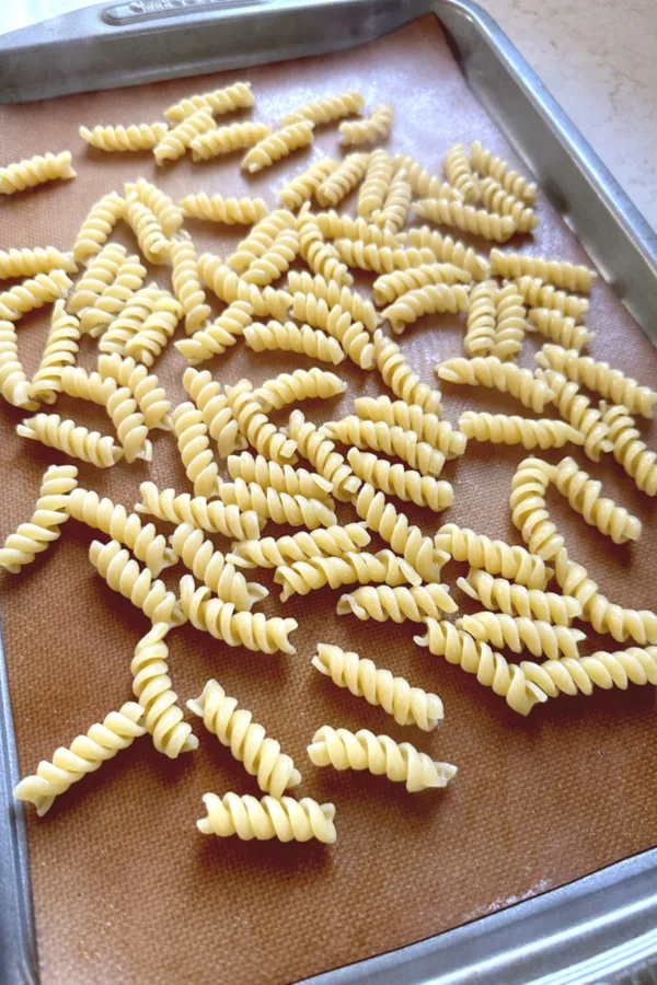 cooked rotini pasta on baking sheet cooling