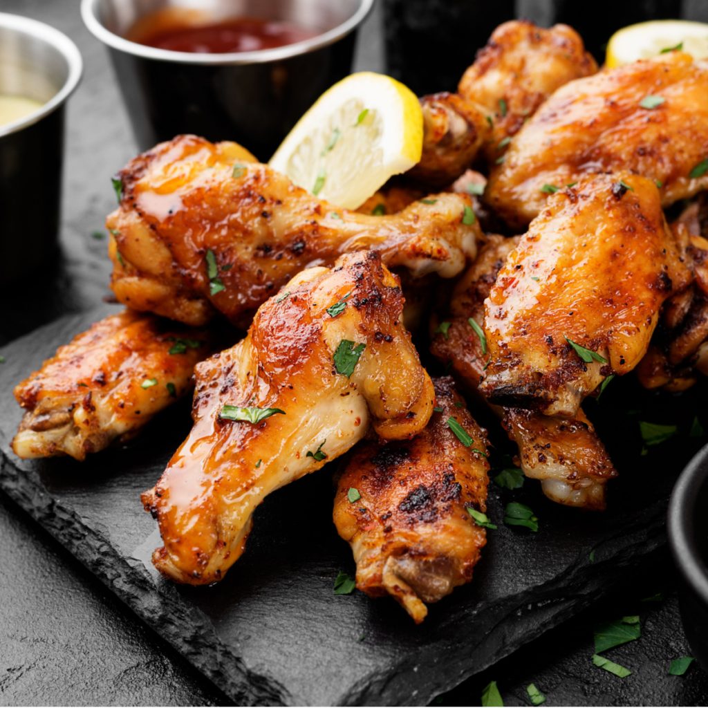 A plate of baked chicken wings with dipping sauce in the background.