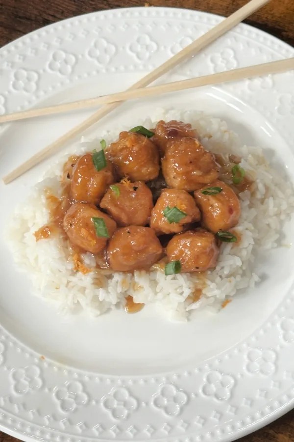 orange chicken on white plate with chopsticks